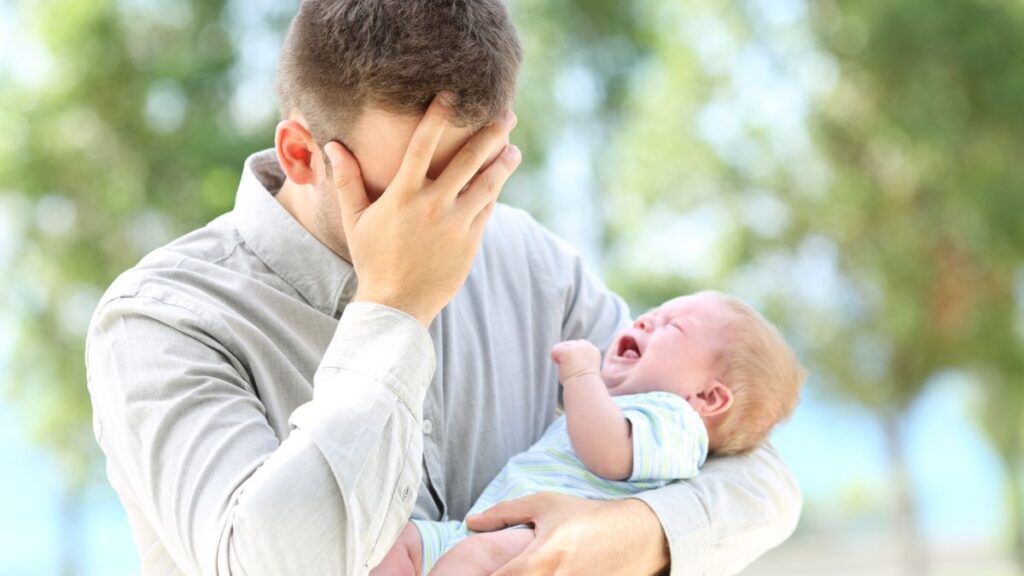 Man holding his face with a crying baby