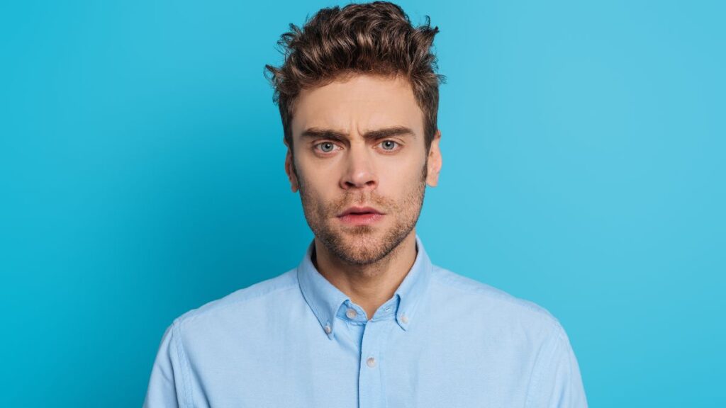 Man in front of a blue background looking confused
