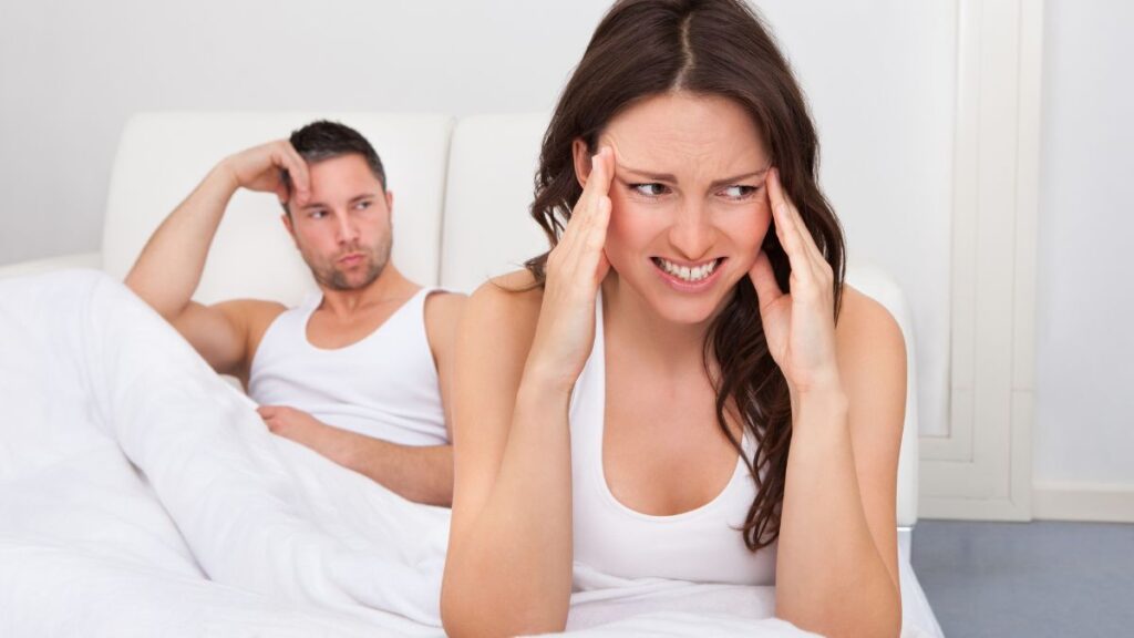 couple fighting in bed both have hands on head looking upset