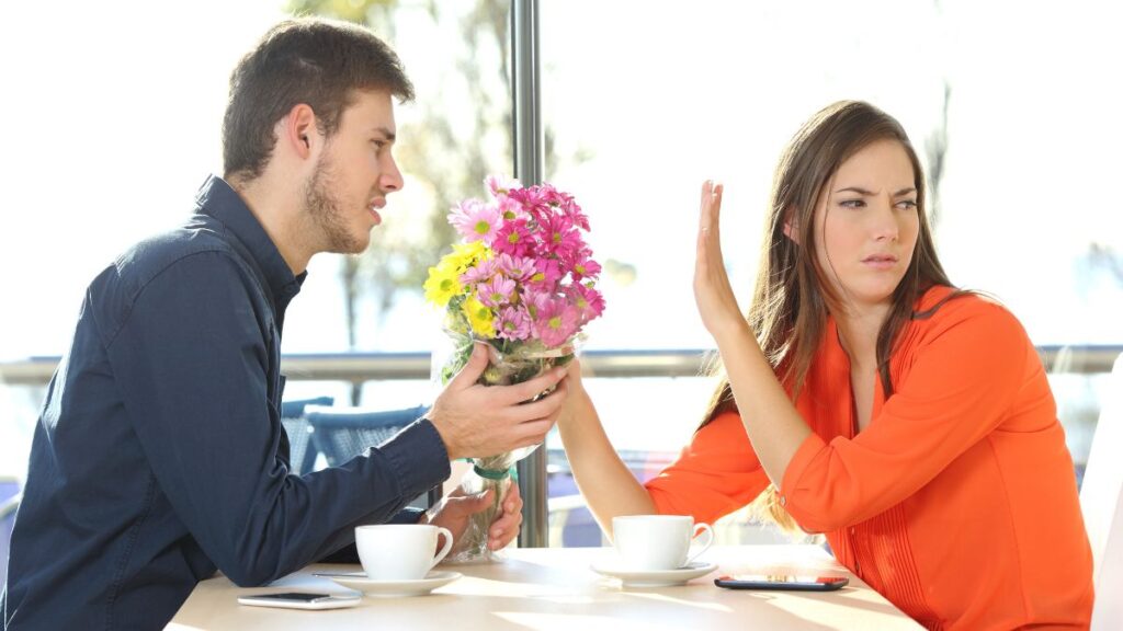 upset couple woman rejecting man at the table with flowers