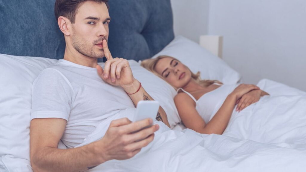 woman sleeping next to man shushing in bed on phone