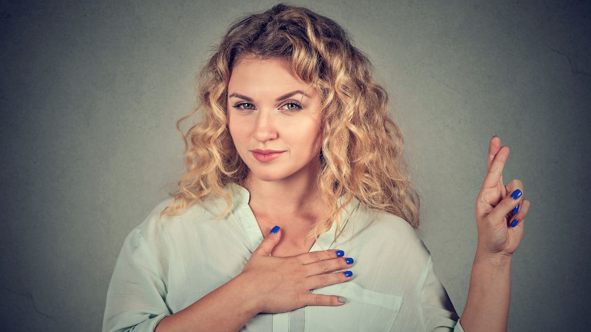 woman with hand on hear and fingers crossed looking shady