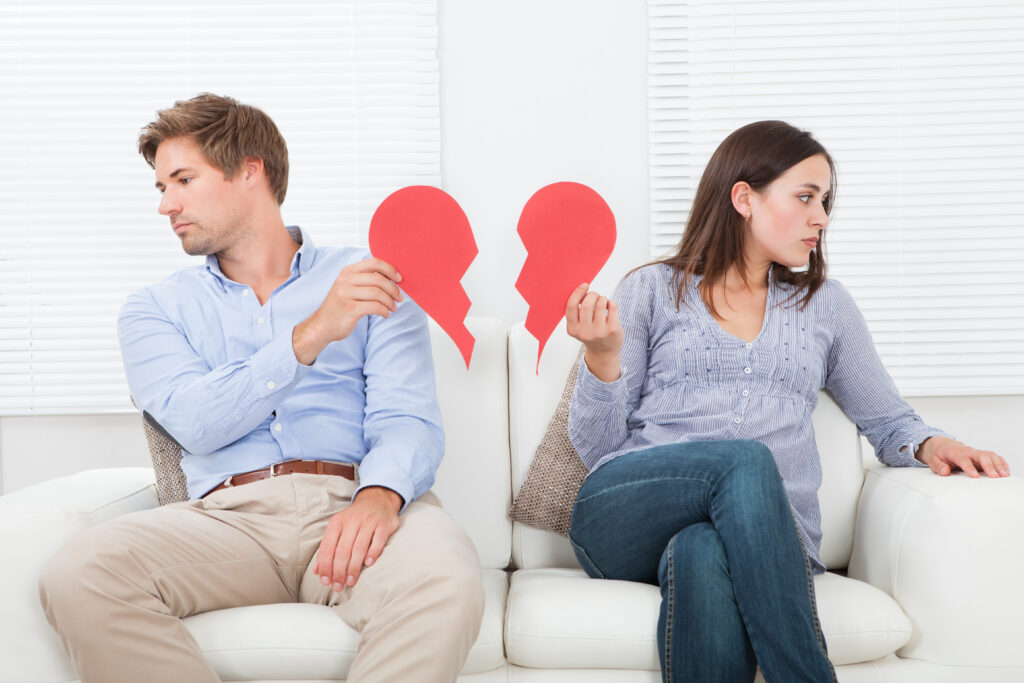 Full length of couple ignoring each other while sitting on sofa at home