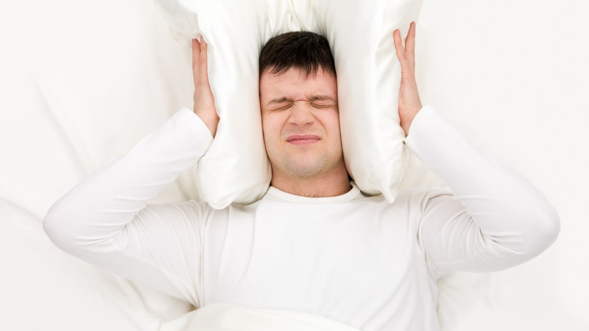 Man in bed covering his ears with his pillow