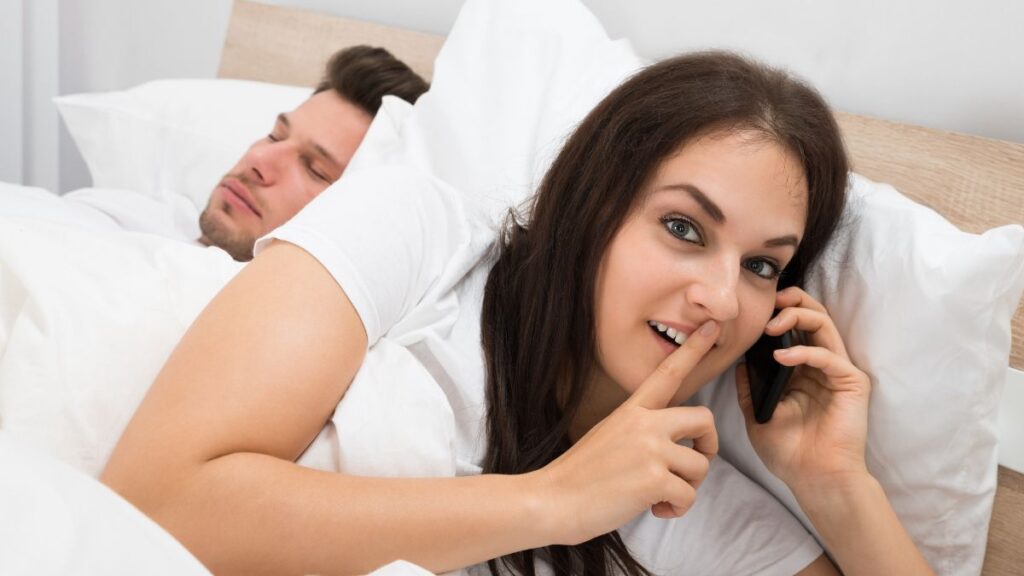 Woman whispering on the phone while a man sleeps beside her