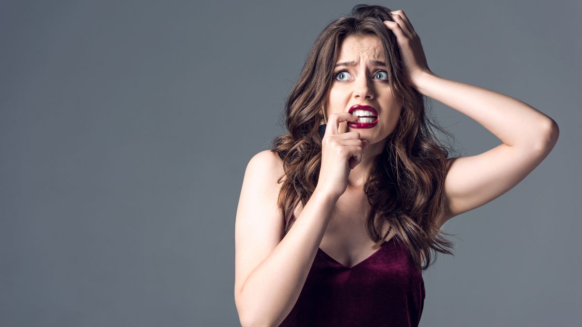 Woman with long brown hair looking scared, biting her nail